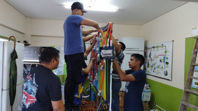 Grupo de alumnos realizando el cableado y conexionado de llaves térmicas y disyuntores sobre un tablero didáctico de simulación en el aula