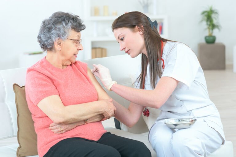 Enfermera con ambos guantes quirúrgicos colocados desinfectando el brazo de una paciente anciana sentada en el sillón antes de aplicar una inyección intramuscular, tal como se muestra en la foto enfermeria...jpg.