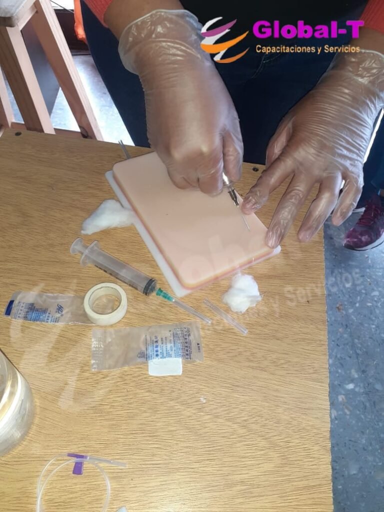 Estudiante con guantes transparentes de vinilo realizando una simulación de punción con aguja sobre una almohadilla didáctica de piel sintética para colocación de vía, rodeada de jeringas, gasas y cinta