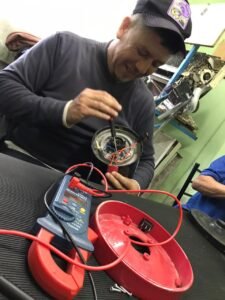 Estudiante utilizando un destornillador para desarmar el motor de un electrodoméstico pequeño junto a una pinza amperométrica digital sobre la mesa del taller