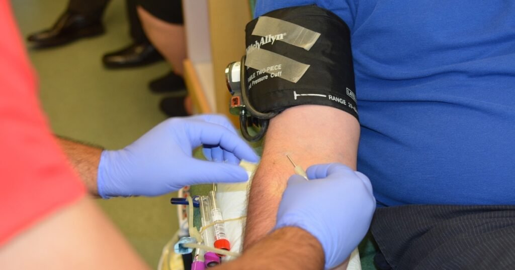Primer plano de un enfermero utilizando guantes de látex azules para realizar una extracción de sangre con aguja en el brazo de un paciente que tiene colocado un brazalete de presión arterial WelchAllyn