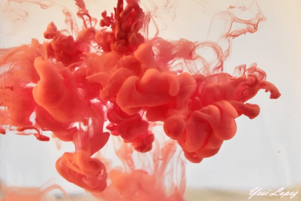 Captura fotográfica macro de alta velocidad que muestra formas abstractas de tinta roja dispersándose y flotando en el agua con fondo blanco