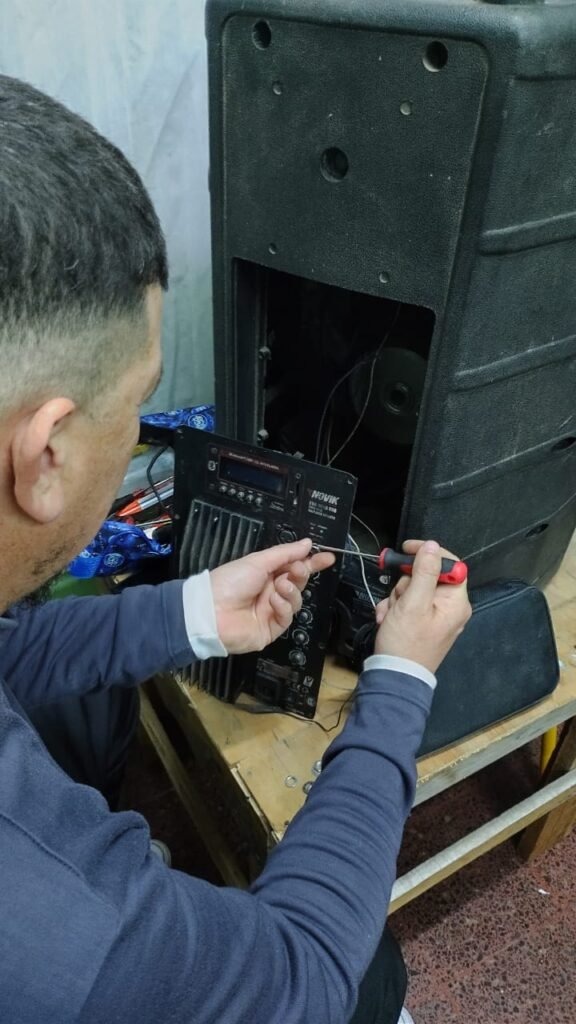 Estudiante utilizando un destornillador de punta Philips para desarmar el panel trasero de conexiones y amplificación de un bafle potenciado marca Novik en el banco de trabajo