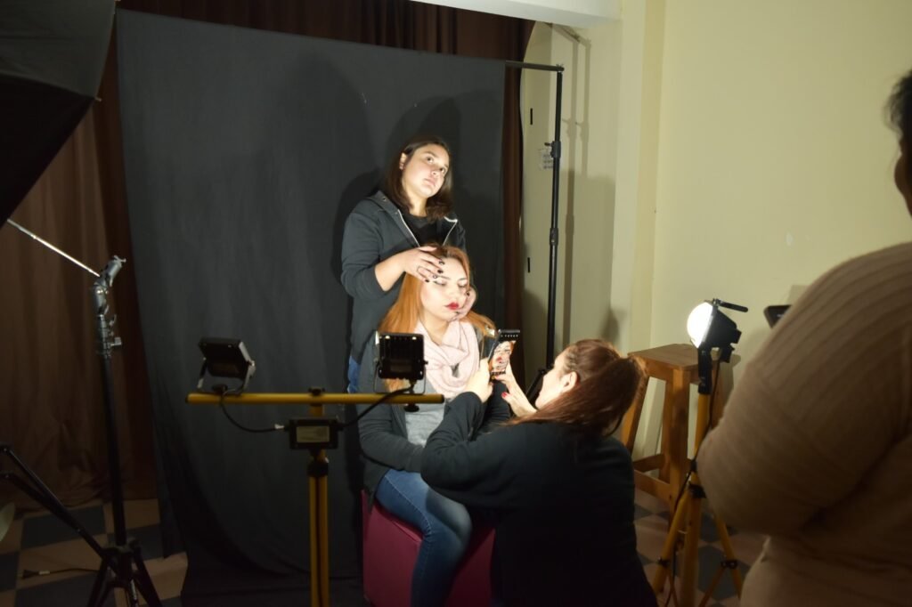 Alumnas y profesor configurando focos de iluminación LED, esquemas de luces y un fondo infinito negro para una sesión de fotos en el taller presencia
